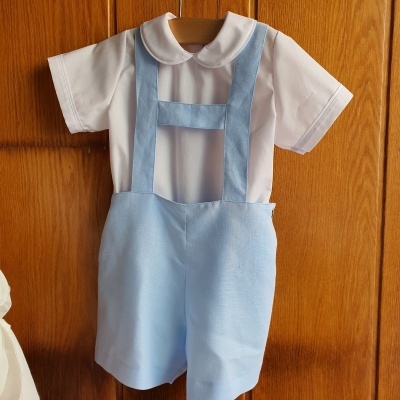 Conjunto de roupa infantil branca e azul pendurado em porta de madeira.