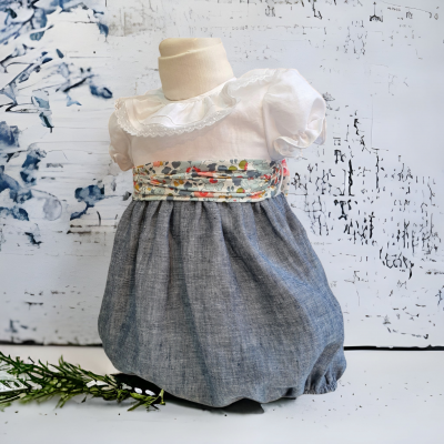 Vestido de bebé branco com parte inferior azul cinzenta e faixa floral colorida ao peito