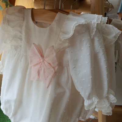 Macacão branco de bebê com laço cor-de-rosa e detalhes de renda