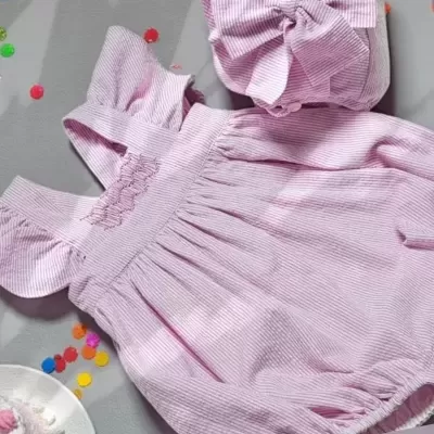 Conjunto rosa claro de vestido e chapéu para bebé com listras e laços grandes.