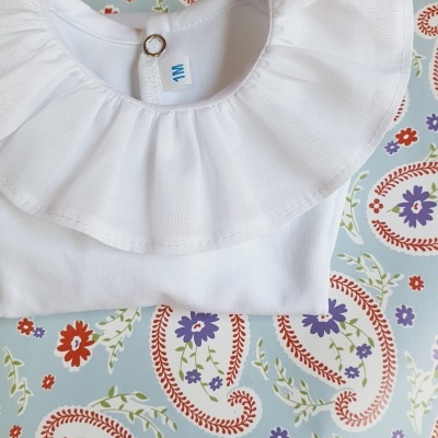 Camisola branca com gola frisada sobre tecido com padrão paisley colorido