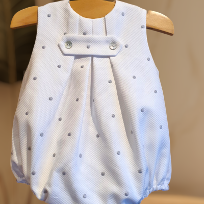 Macacão de bebé branco com pontos cinzentos e botões prateados, pendurado em cabide de madeira
