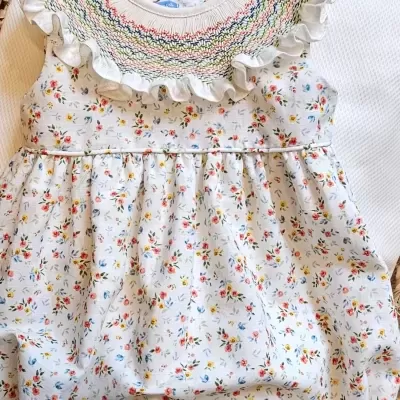 Macacão de bebé branco com padrão floral colorido e gola bordada com volante.