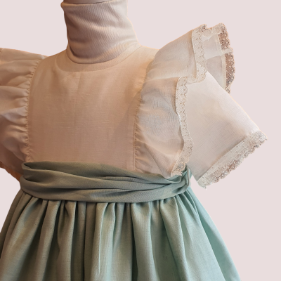 Vestido de criança bege com mangas bufantes brancas rendadas e saia verde-água plissada.