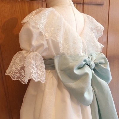 Vestido branco com renda delicada e faixa azul claro amarrada em laço