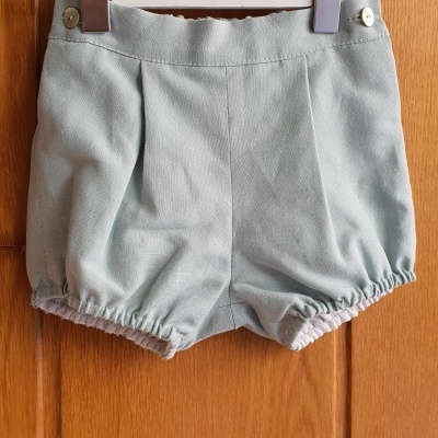 Calções de bebé azuis claros pendurados numa cabide numa porta de madeira.