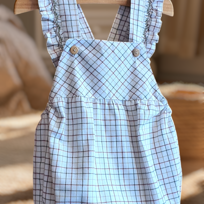 Macacão de bebé branco com padrão de quadrícula castanha e alças com folhos pendurado