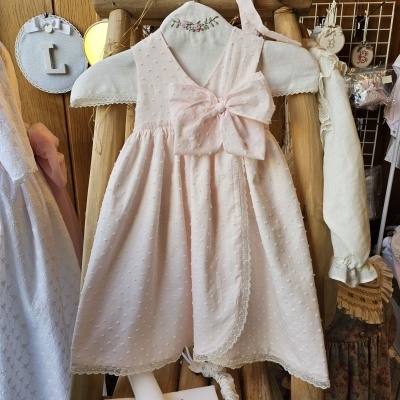 Vestido rosa claro de criança com laço e renda, pendurado em cabide forrado com bordado de flores