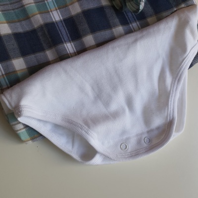 Body branco de algodão com fecho de pressão, sobre tecido xadrez azul e bege