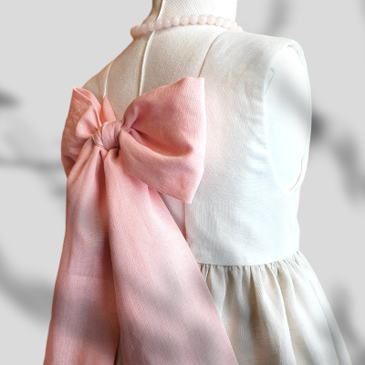 Vestido branco de menina com grande laço rosa nas costas e colar de contas rosa em manequim