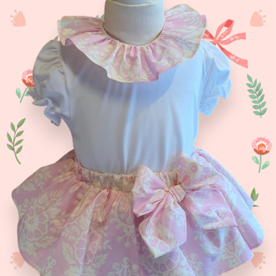 Vestido infantil branco e rosa com padrão floral e laço decorativo.
