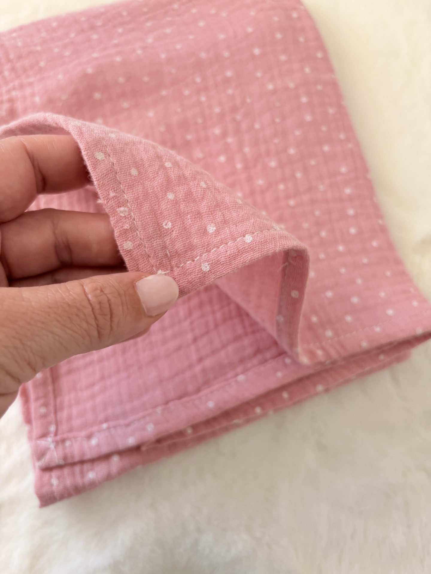 Fralda musselina rosa cereja com pintinhas brancas Pano rosa com bolinhas brancas segurado por mão sobre superfície branca