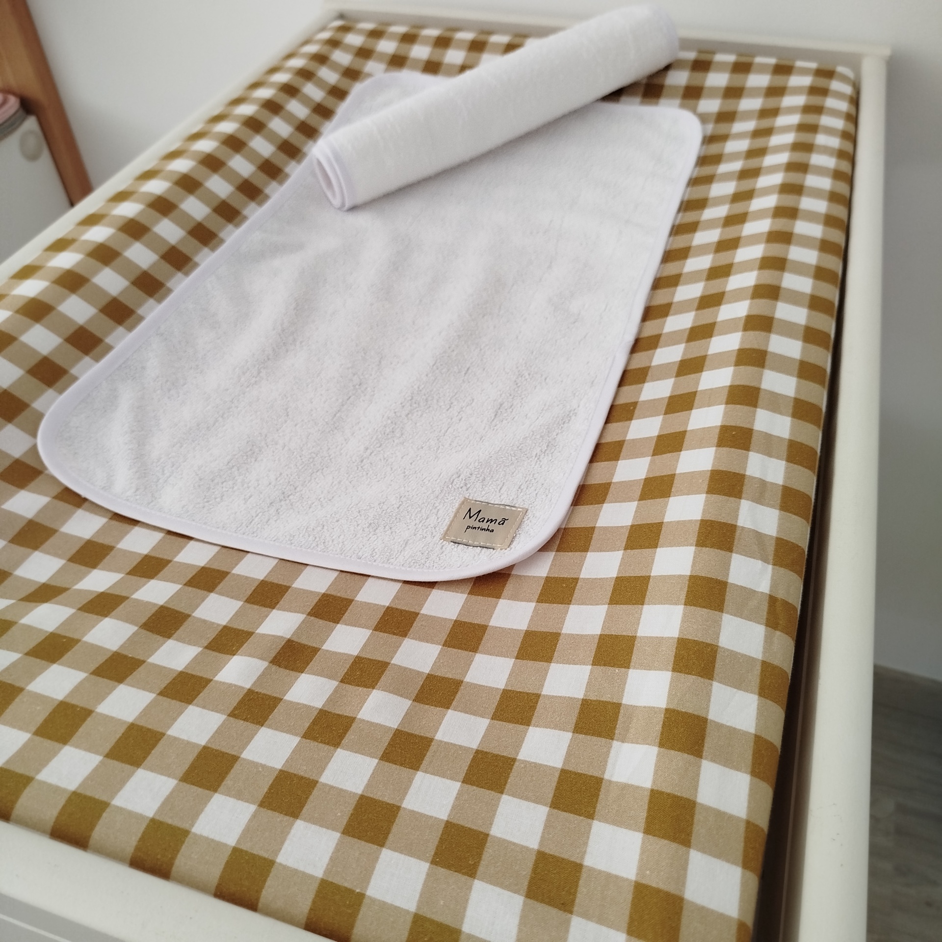 Forra para Trocador de fralda | muda fraldas | forra para muda fraldas | vichy mostarda| quadrados Tapete branco com etiqueta sobre superfície xadrez bege e branca em móvel branco