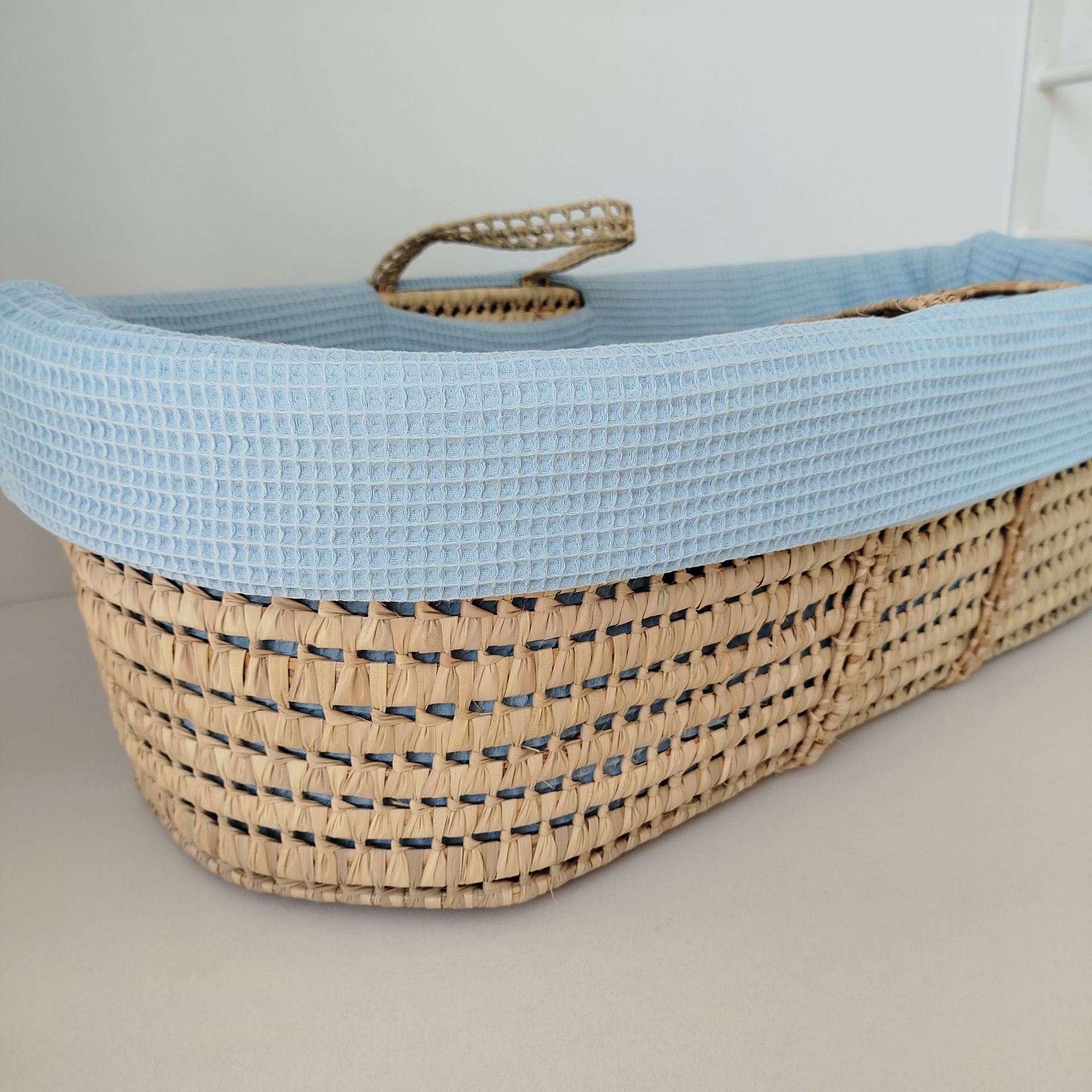 Forra para alcofa | alcofa de verga | berço bebé | waffle azul Cesto de vime com forro azul claro sobre superfície branca