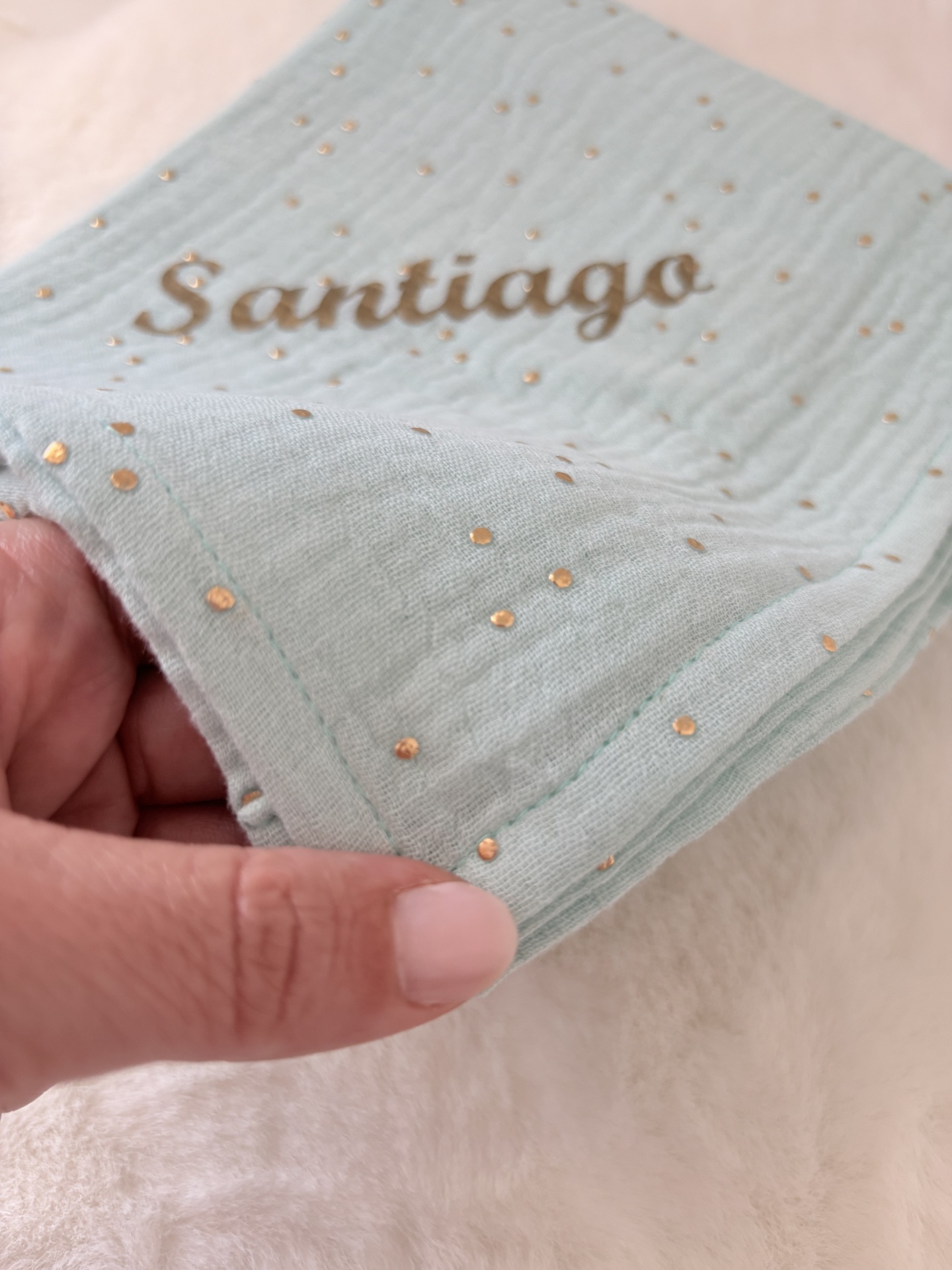 Fralda musselina verde água com pintinhas douradas com nome Santiago Pano verde-água com pontos dourados e texto Santiago impresso em dourado