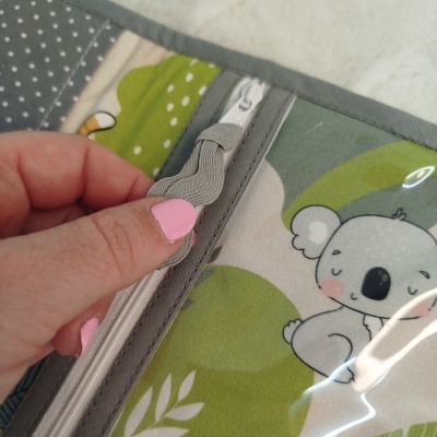 Estojo com desenho de coala cinzento e fecho zip cinzento, com mão segurando o fecho.