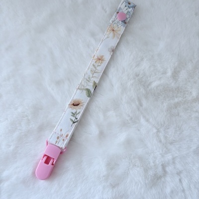Tira de tecido com padrão floral e clip rosa sobre superfície branca peluda