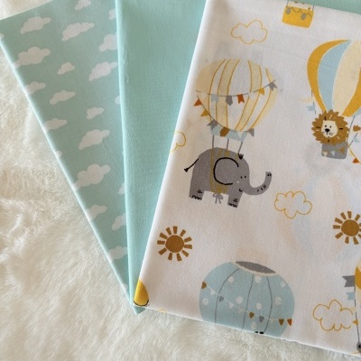 Três tecidos infantis com nuvens e balões de ar quente sobre fundo branco.