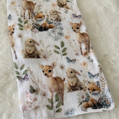 Pano de tecido branco com estampado de desenhos infantis de animais e flores.