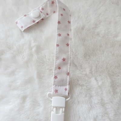 Prendedor de chupeta branco com estrelas cor-de-rosa e fecho plástico em fundo felpudo branco