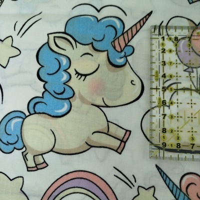 Pano branco com padrão infantil de unicórnio, estrelas e arco-íris e régua para medir.