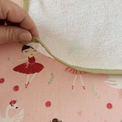 Toalha branca com bordas verdes sobre tecido rosa com desenhos de bailarinas e cisnes