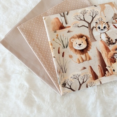 Três tecidos castanhos claros com padrões, incluindo desenhos de animais da savana, sobre superfície branca felpuda.