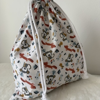 Saco de tecido branco com padrão de animais coloridos e cordões brancos