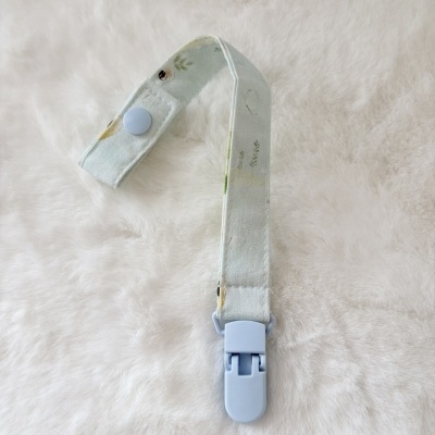 Fita com padrão floral e presilha azul clara sobre fundo branco peludo.