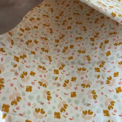Tecido floral com padrão castanho, verde e rosa e botão de pressão branco.