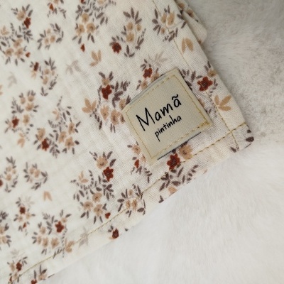 Pano branco com flores castanho-bege e etiqueta Mamã pintinha sobre superfície felpuda branca