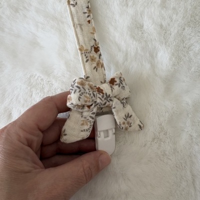 Tira para chupeta em tecido bege floral com laço e clip branco
