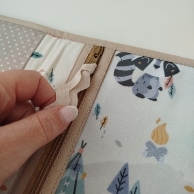 Capa protetora em tecido com padrão de guaxinim, fogueira, folhas e tendas em tons pastel