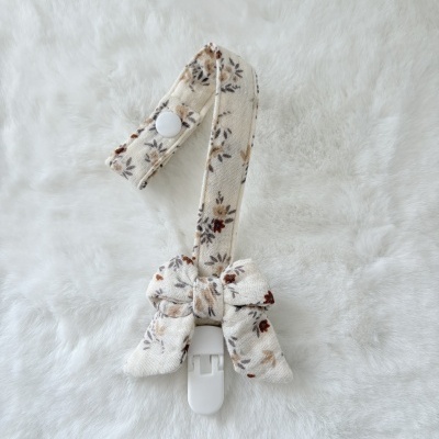 Presilha para chupeta em tecido com padrão floral e botão branco sobre fundo felpudo branco