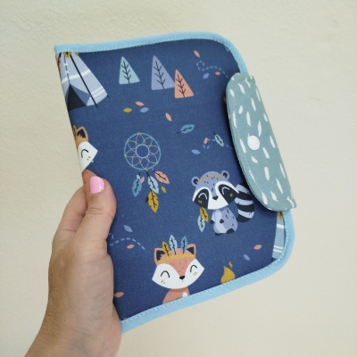 Carteira de tecido com estampado azul e animaizinhos, segurada por mão feminina