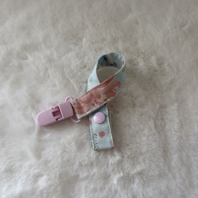 Mordedor ou prendedor de chupeta floral e rosa sobre superfície branca felpuda