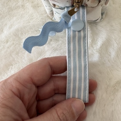 Fecho de mala com alça azul riscada e botão azul sobre tecido floral