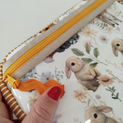 Estojo com estampado de coelhos e flores, zíper amarelo e puxador laranja.