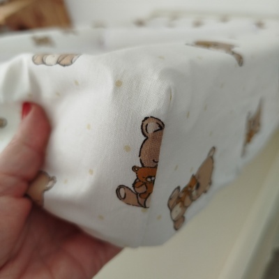 Lençol branco com padrão de ursos castanhos suave sendo segurado por uma mão.