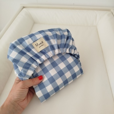 Touca de tecido azul e branco xadrez com etiqueta Mamã pintinha, segurada por mão com unhas vermelhas