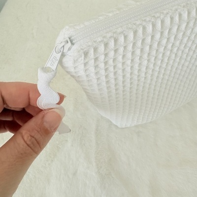 Bolsa branca com textura e fecho em fundo branco.