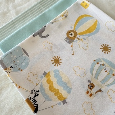 Três panos de tecido para bebé com padrões diferentes, um liso azul claro, um às riscas, e um estampado com balões de ar quente e animais.