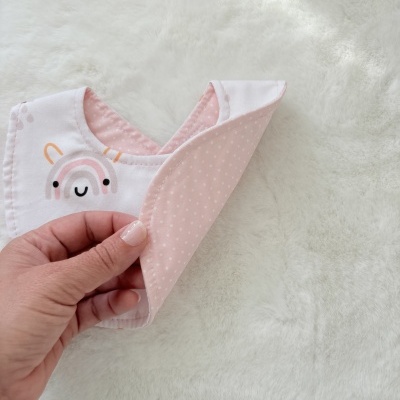 Babete de tecido duplo rosa e branco com arco-íris sorridente e padrão de bolinhas
