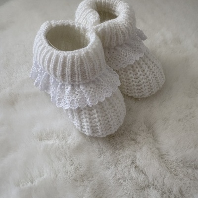 Sapatinhos de bebé tricô branco com renda sobre superfície felpuda clara