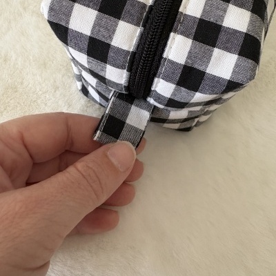 Estojo xadrez preto e branco com zipper negro numa superfície clara