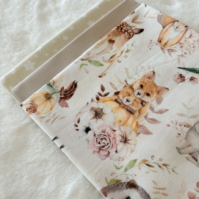 Tecidos dobrados com padrões de animais, estrelas e cor cinza, sobre superfície felpuda branca.