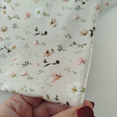 Tecido floral creme com padrão de flores em tons pastéis e costura, segurado por mão com unhas vermelhas.