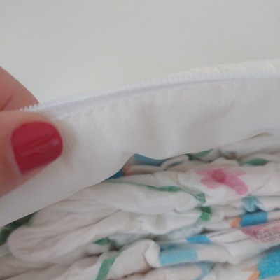 Pano branco com textura suave numa mão com unhas vermelhas sobre tecidos coloridos desfocados