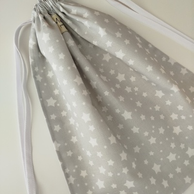 Saco de tecido cinzento com estrelas brancas e fecho de cordões brancos