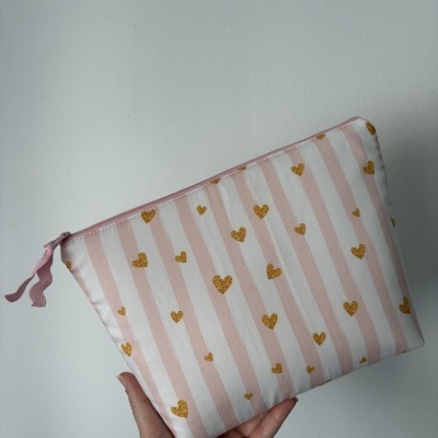 Bolsa ou estojo às riscas rosa e branco com corações dourados e zipper rosa segurado por uma mão